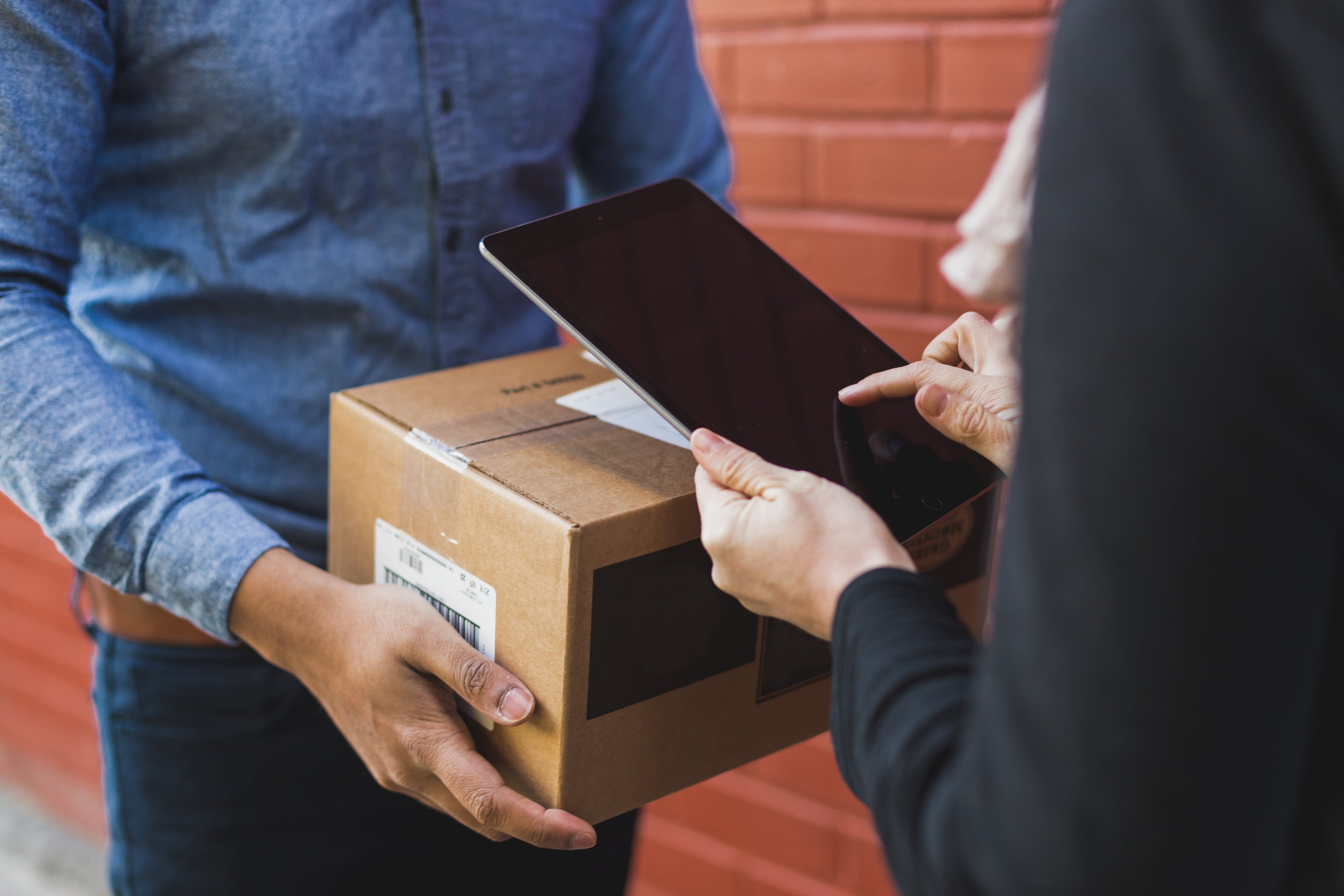 Person receiving a package from another person using a tablet for verification.